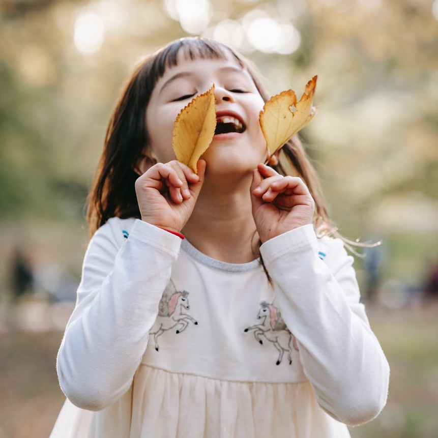 little girl in unicorn dress smiling and playing with leaves